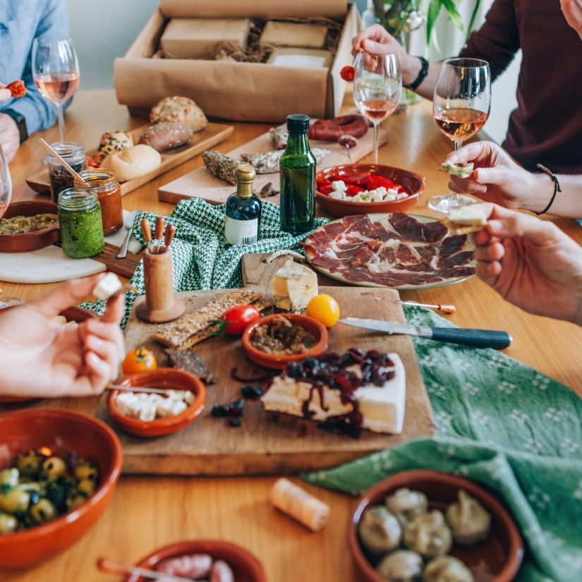 unrecognizable people sitting around a table full of goodies - friends have an aperitif from food box delivered